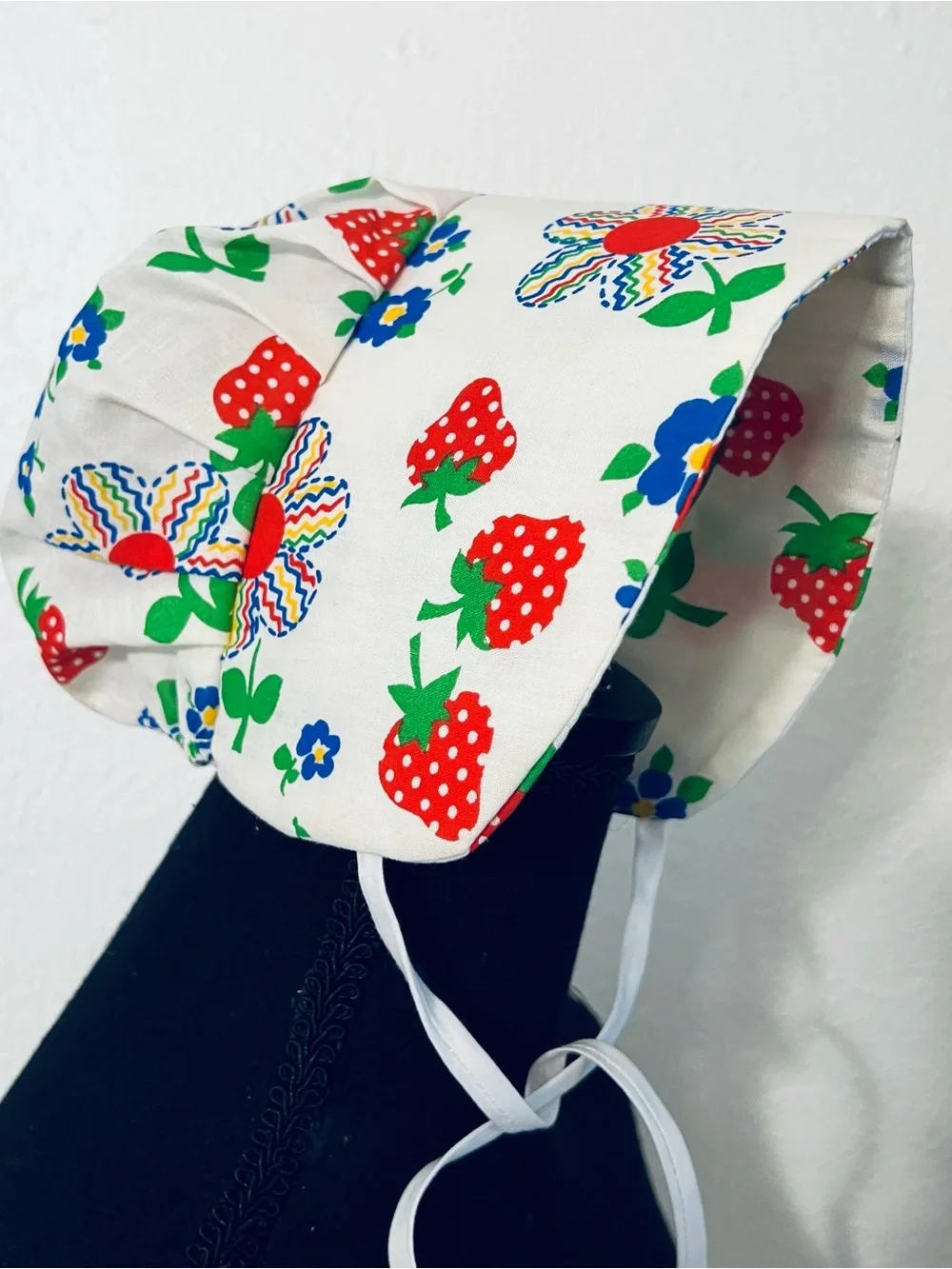 Charming vintage-style baby sunbonnet features a playful white fabric patterned